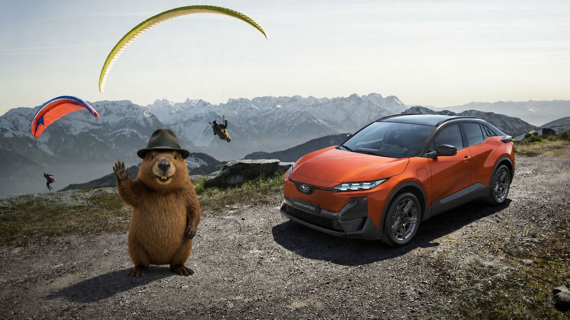 Hans Murmeli winkt neben einem orangefarbenen Subaru Uncharted in den Alpen.